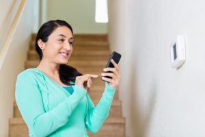 woman-uses-phone-to-adjust-smart-thermostat